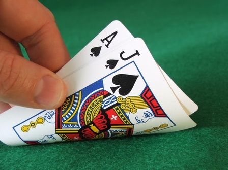 A left thumb and index finger pull back the ace and jack of spades
