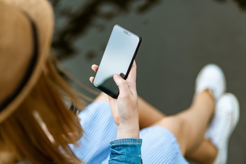 A woman holds a black smartphone in her right hand and uses it to play games with cash funds at the best slot sites