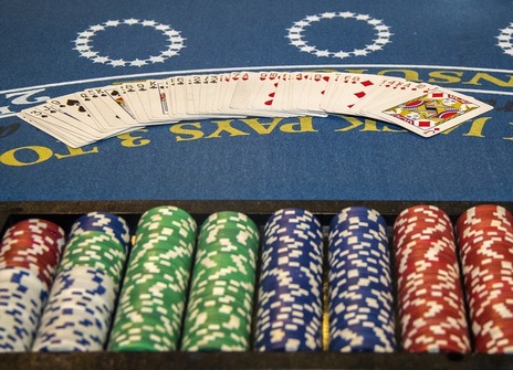 Eight piles of white, red, green, and blue poker chips are lined up in front of a deck of cards spread across a blue betting table