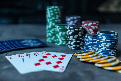 The ace, king, queen, jack, and ten of diamonds make a royal flush in front of piles of green, blue, black, red, and yellow poker chips